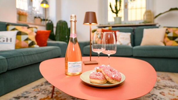 A cozy living room with a green sofa, a round table with a bottle of champagne, two wine glasses, and a plate of donuts. - MGH Luxury - Sunset Lakeview House Desenzano (Desenzano del Garda)