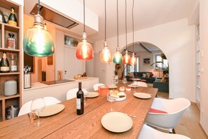 A modern dining area with a wooden table set for a meal, surrounded by white chairs. - MGH Luxury - Sunset Lakeview House Desenzano (Desenzano del Garda)