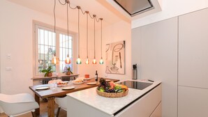 A modern kitchen with a central island, wooden chairs, a fruit bowl, and pendant lighting. - MGH Luxury - Sunset Lakeview House Desenzano (Desenzano del Garda)