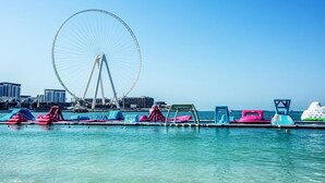 A waterfront area with a large Ferris wheel, colorful floating platforms with seating, and a clear view of the city skyline in the background. - Serene 1-bedroom apartment in Dubai perfect for your getaway (Dubai)
