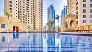 A swimming pool with clear blue water, surrounded by high-rise buildings and palm trees. - Serene 1-bedroom apartment in Dubai perfect for your getaway (Dubai)