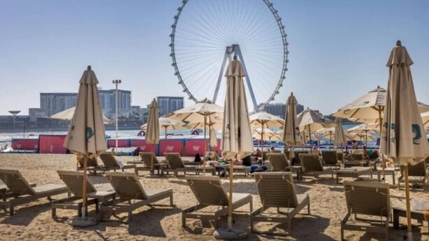 A beach with rows of sun loungers and umbrellas, a Ferris wheel in the background, and a city skyline. - Serene 1-bedroom apartment in Dubai perfect for your getaway (Dubai)