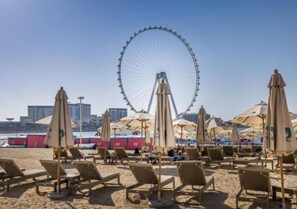 A beach with rows of sun loungers and umbrellas, a Ferris wheel in the background, and a city skyline. - Serene 1-bedroom apartment in Dubai perfect for your getaway (Dubai)
