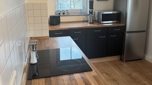 Eine moderne Küche mit Holzarbeitsplatte, schwarzen Schränken, einem Edelstahlkühlschrank und einem Fenster mit Blick auf Gebäude.