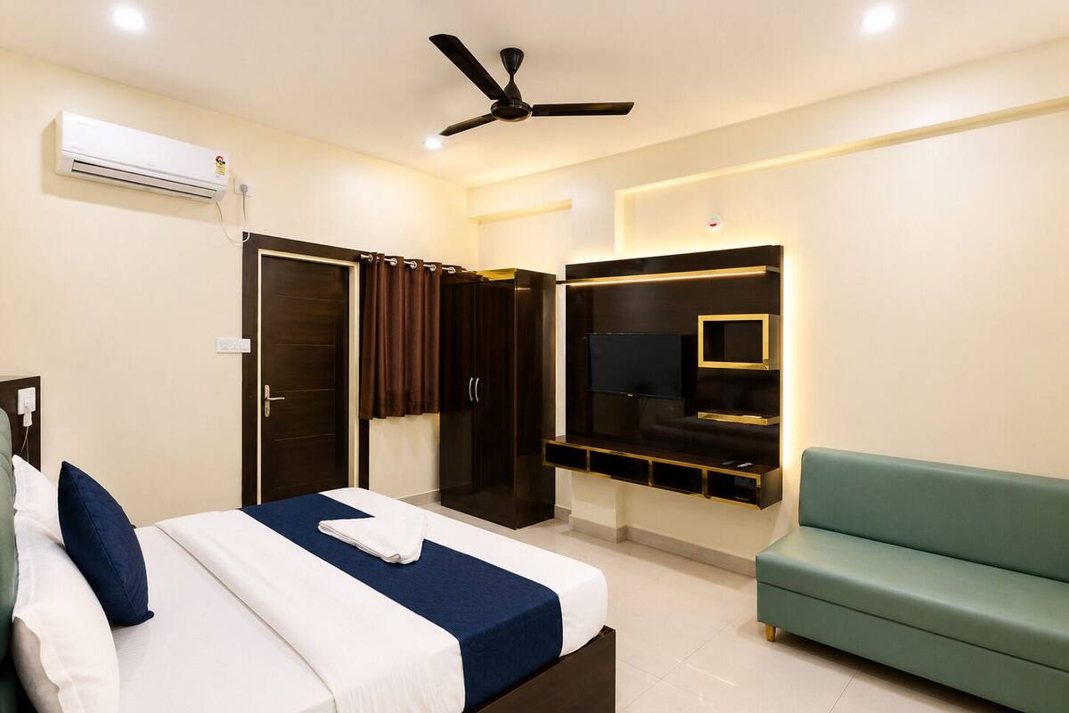 Habitación de hotel con cama, televisor montado en la pared, ventilador de techo y sofá verde.