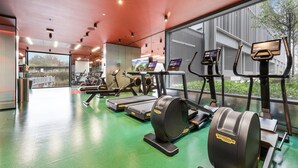 Una palestra moderna con macchinari cardio, postazioni per pesi e un'ampia vetrata che offre vista sull'esterno.