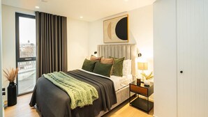 Una camera da letto moderna con un letto, un comodino e vista sulla città attraverso una grande finestra.