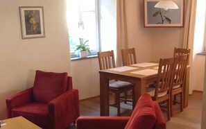 Et spiseområde med et træbord og stole, en rød lænestol og et billede i ramme på væggen.