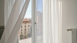 A room with a large window, white curtains, and a view of buildings outside. - Italianway Comfort - Certosa 19 (Milan)