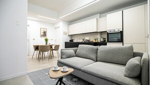 A modern living room with a grey sofa, a small wooden table with a cup, and a dining area with a table and chairs. - Italianway Comfort - Certosa 19 (Milan)