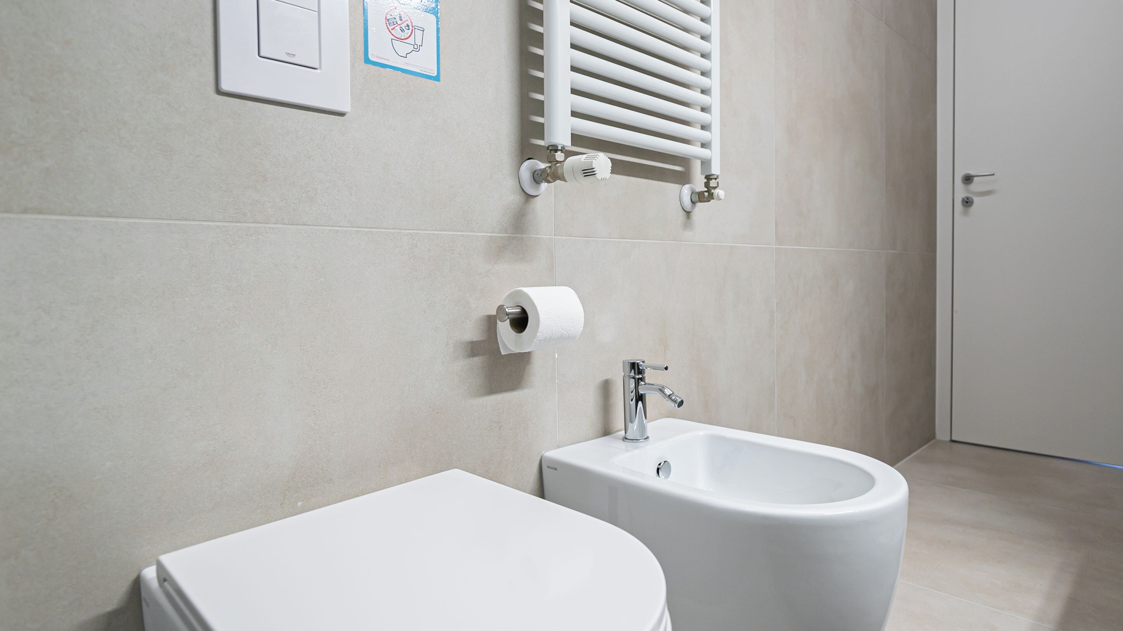 A modern bathroom with a toilet, bidet, and towel rack.