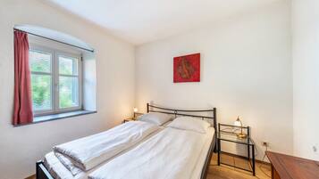 Une chambre avec deux lits, une fenêtre avec des rideaux, une table de chevet avec une lampe et une œuvre d’art rouge accrochée au mur.