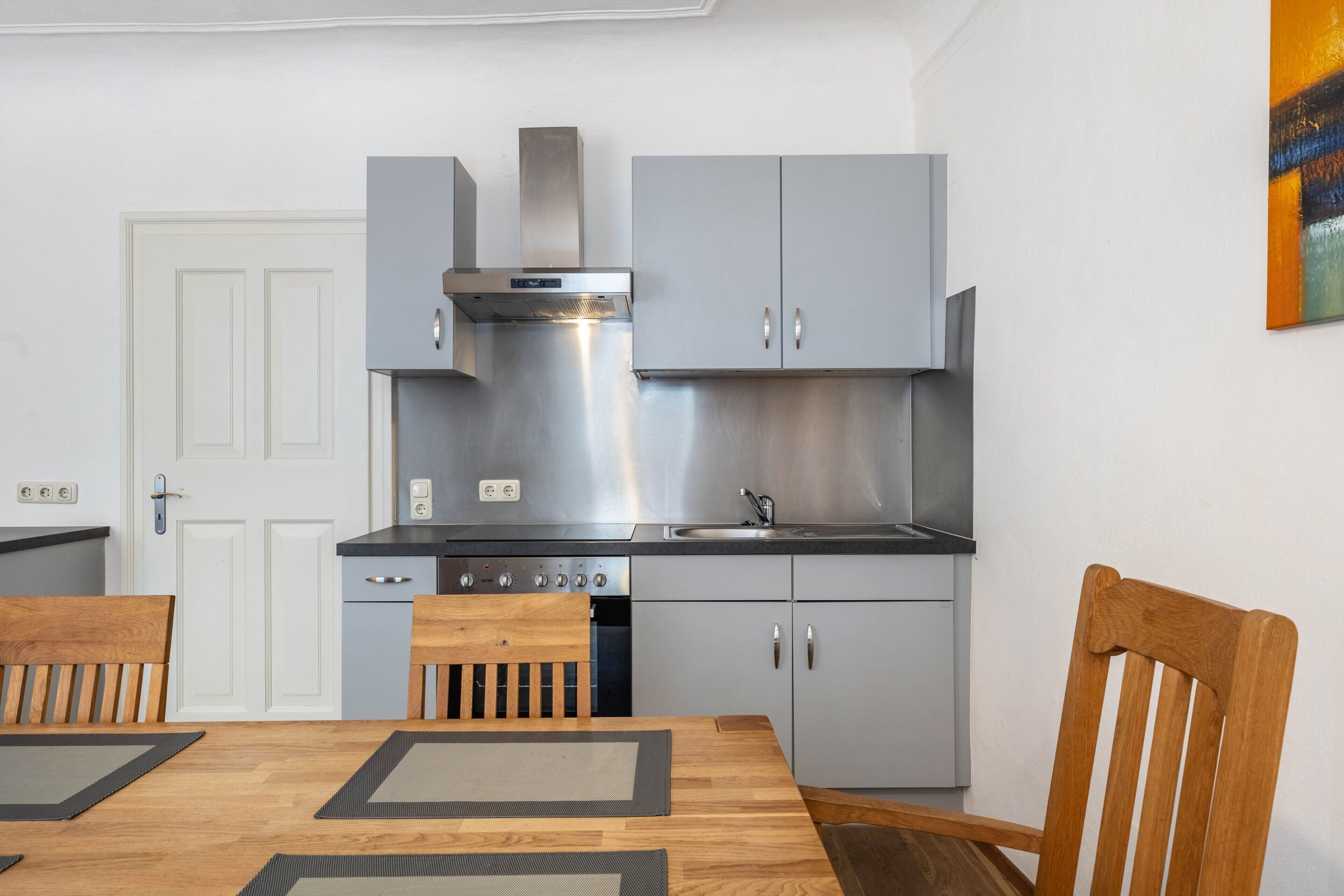 Una cocina moderna con gabinetes grises, electrodomésticos de acero inoxidable y una mesa de comedor de madera con sillas.