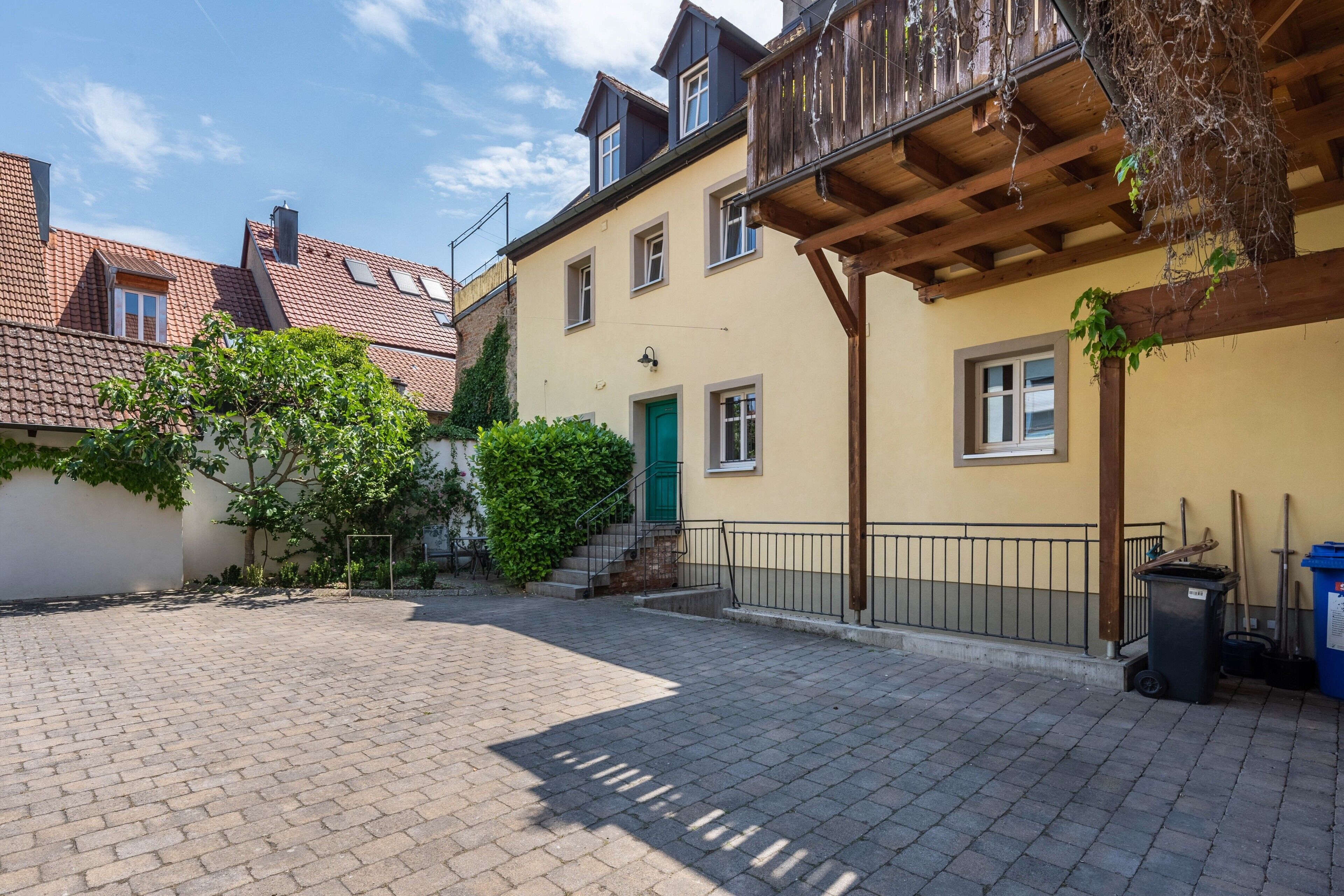 A courtyard with a paved walkway, a green door, and a balcony with wooden railings.