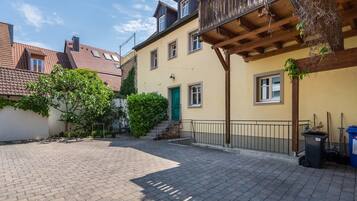 A courtyard with a paved walkway, a green door, and a balcony with wooden railings.