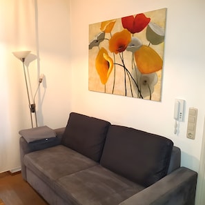 Una sala de estar con un sofá gris, una lámpara de pie y un cuadro de flores colgado en la pared.