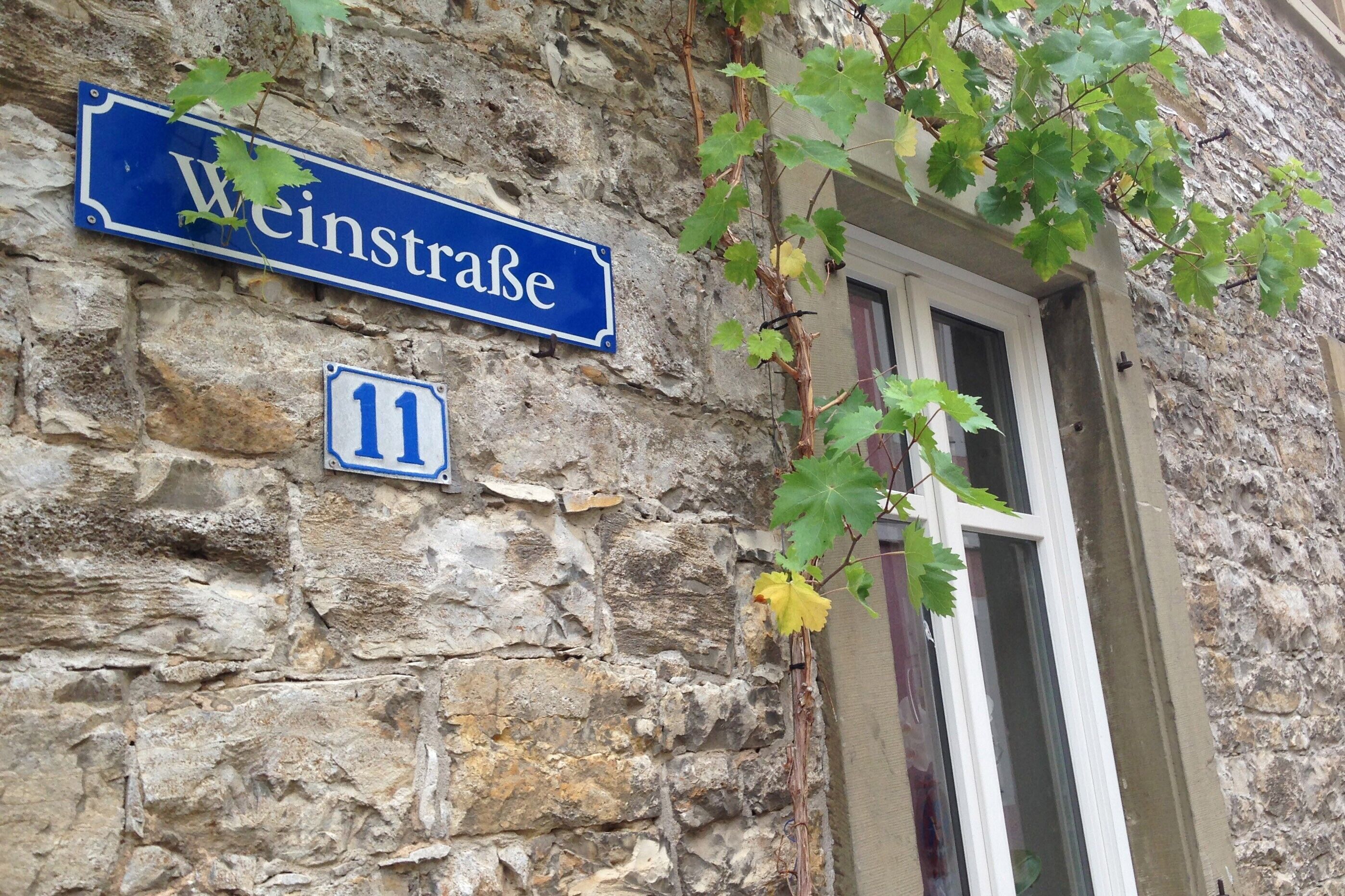 Un bâtiment en pierre, avec une plaque de rue bleue indiquant « Weinstrasse » et une plus petite plaque portant le numéro « 11 ».