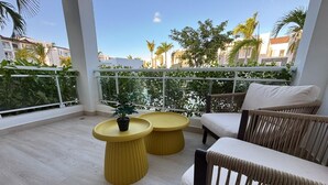 En balkon med to gule runde borde, en hvid sofa med hynder og en potteplante.