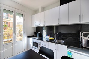 Eine kompakte Küche mit weißen Schränken, einer schwarzen Arbeitsplatte, einem Edelstahlspülbecken und einer Kaffeemaschine.