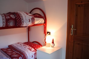 A bunk bed with patterned bedding, a bedside table with a lamp, and a wooden door.