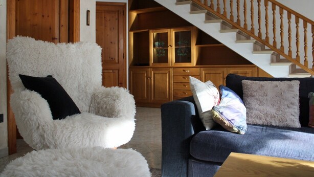 A living room with a white furry chair, a blue sofa with pillows, wooden cabinets, and a wooden staircase. - Apartment 'The Wild Deer Retreat' with Mountain View and Balcony (Schilpario)