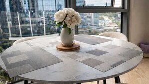 Ein runder Tisch mit einer Blumenvase, vier Stühlen und Blick auf die Stadt durch große Fenster.