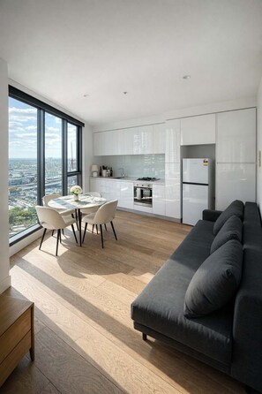 Eine moderne Küche mit weißen Schränken, einem Esstisch mit Stühlen, einer Couch und Blick auf die Stadt.