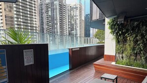 A rooftop terrace with a pool, wooden deck, lounge chairs, and a view of tall buildings. - Skyline Stays | L22 1BR Free Parking near Crwon (Southbank)