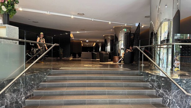 A hotel lobby with marble stairs, a reception desk, and a modern interior design. - Skyline Stays | L22 1BR Free Parking near Crwon (Southbank)