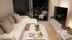 A modern living room with a sofa, a coffee table, a TV, and a balcony with a city view. - Skyline Stays | L22 1BR Free Parking near Crwon (Southbank)