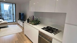 A modern kitchen with white cabinetry, a gas stove, and a built-in oven. There is a large window providing a view of the city. - Skyline Stays | L22 1BR Free Parking near Crwon (Southbank)
