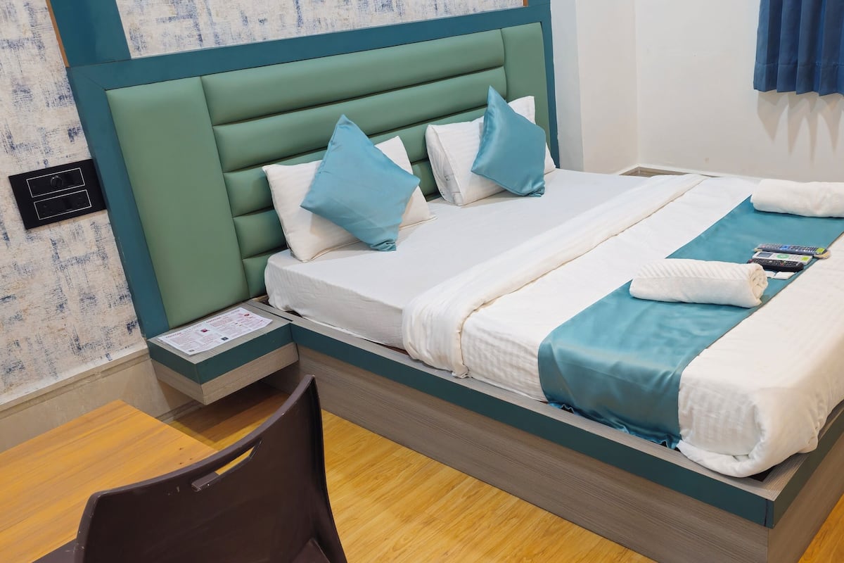 A neatly made bed with a teal headboard, white and teal bedding, and a pair of towels.