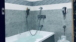 Ein modernes Badezimmer mit einer freistehenden Badewanne, einer Handbrause und einem am Wand montierten Wasserhahn.