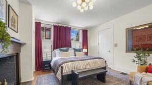 Ein Schlafzimmer mit Bett, Nachttisch, Kamin und einem großen Fenster mit Vorhängen.