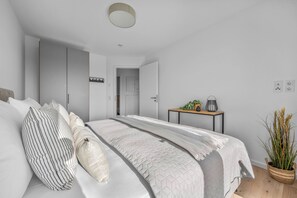 A modern bedroom with a bed, bedside tables, and a door leading to another room. - The View C05 Sonnengruß - Balcony, garden furniture, shared. Sauna, car park (Dagebüll)