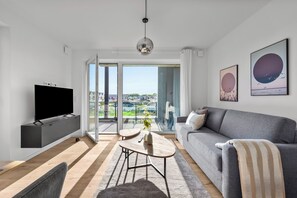 Ein modernes Wohnzimmer mit Flachbildfernseher, grauem Sofa und einem großen Fenster mit Blick auf die Stadt.