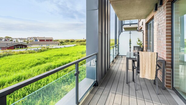 A balcony with a view of a green field, a brick building, and a clear sky. - The View C05 Sonnengruß - Balcony, garden furniture, shared. Sauna, car park (Dagebüll)