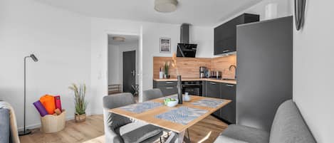 A modern kitchen with a built-in stove, a dining area with a table and chairs, and a living area with a sofa.