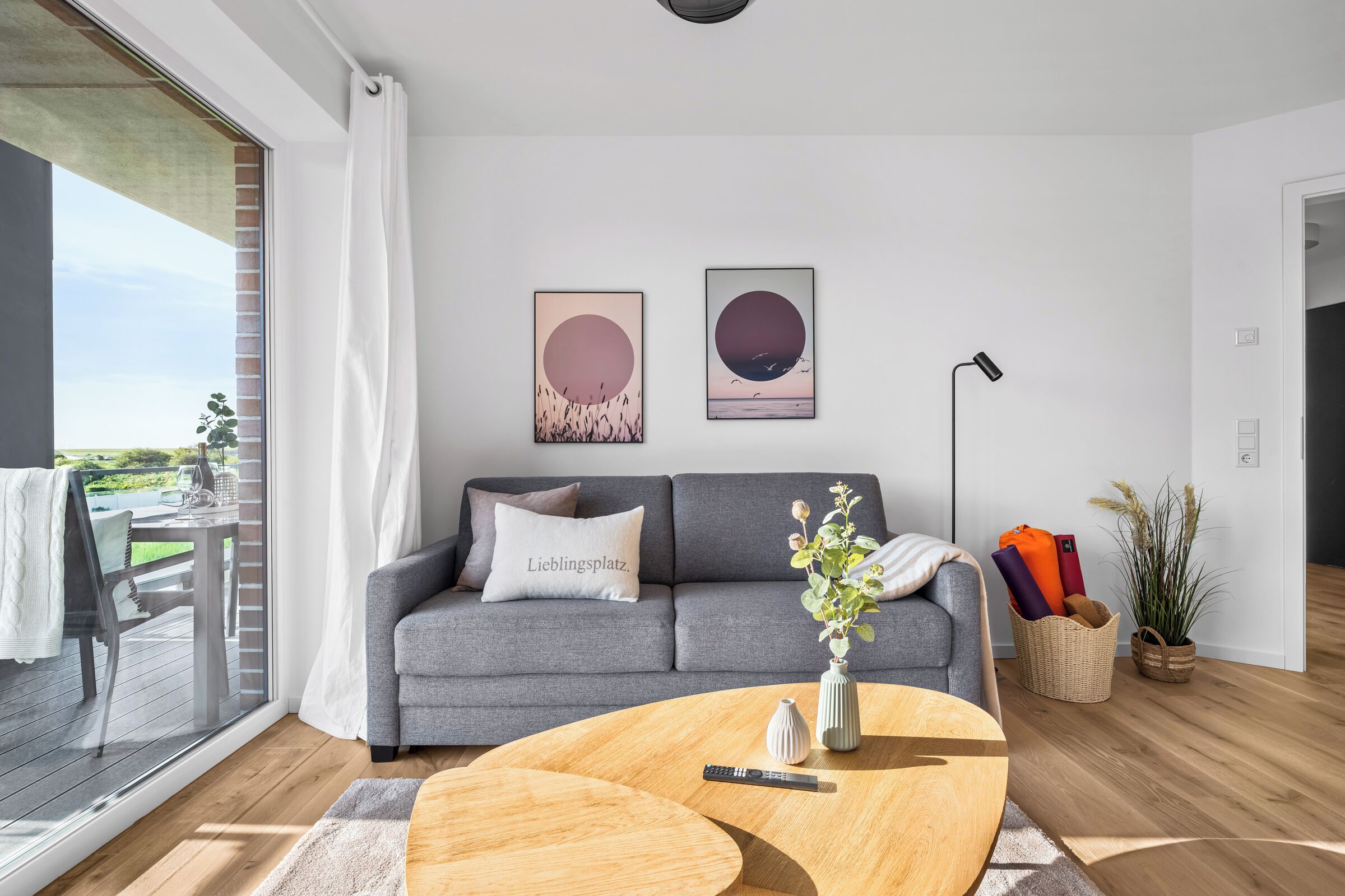 Un salon moderne avec un canapé gris, une table basse et une grande fenêtre donnant sur un balcon.