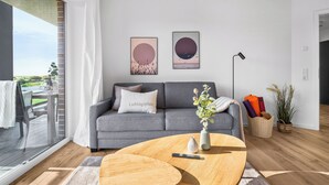 A modern living room with a grey sofa, a coffee table, and a large window overlooking a balcony. - The View C05 Sonnengruß - Balcony, garden furniture, shared. Sauna, car park (Dagebüll)