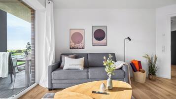 Un salon moderne avec un canapé gris, une table basse et une grande fenêtre donnant sur un balcon.