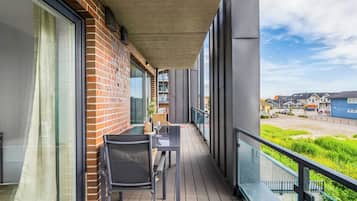 Un balcon avec une table et des chaises, un mur en briques et une vue sur un quartier résidentiel.