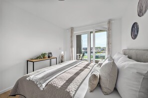 Ein Schlafzimmer mit Bett, Nachttisch, Fenster mit Vorhängen und Blick ins Freie.