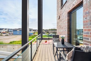 A balcony with a wooden deck, a table, and a chair. - The View C05 Sonnengruß - Balcony, garden furniture, shared. Sauna, car park (Dagebüll)