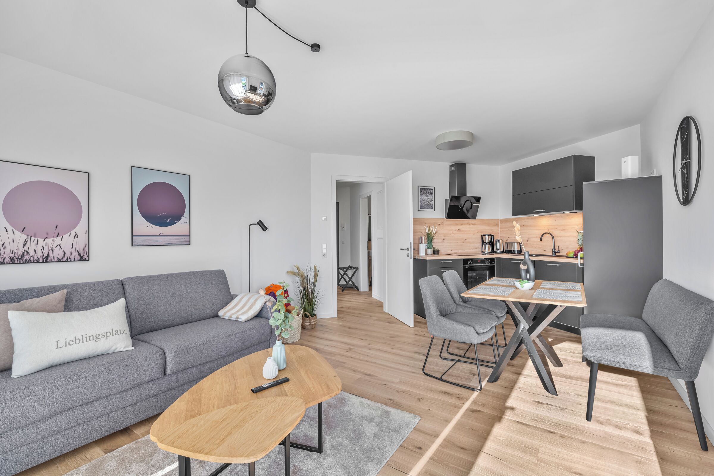 Een moderne woonkamer met een grijze bank, een houten salontafel en een eethoek met grijze stoelen.