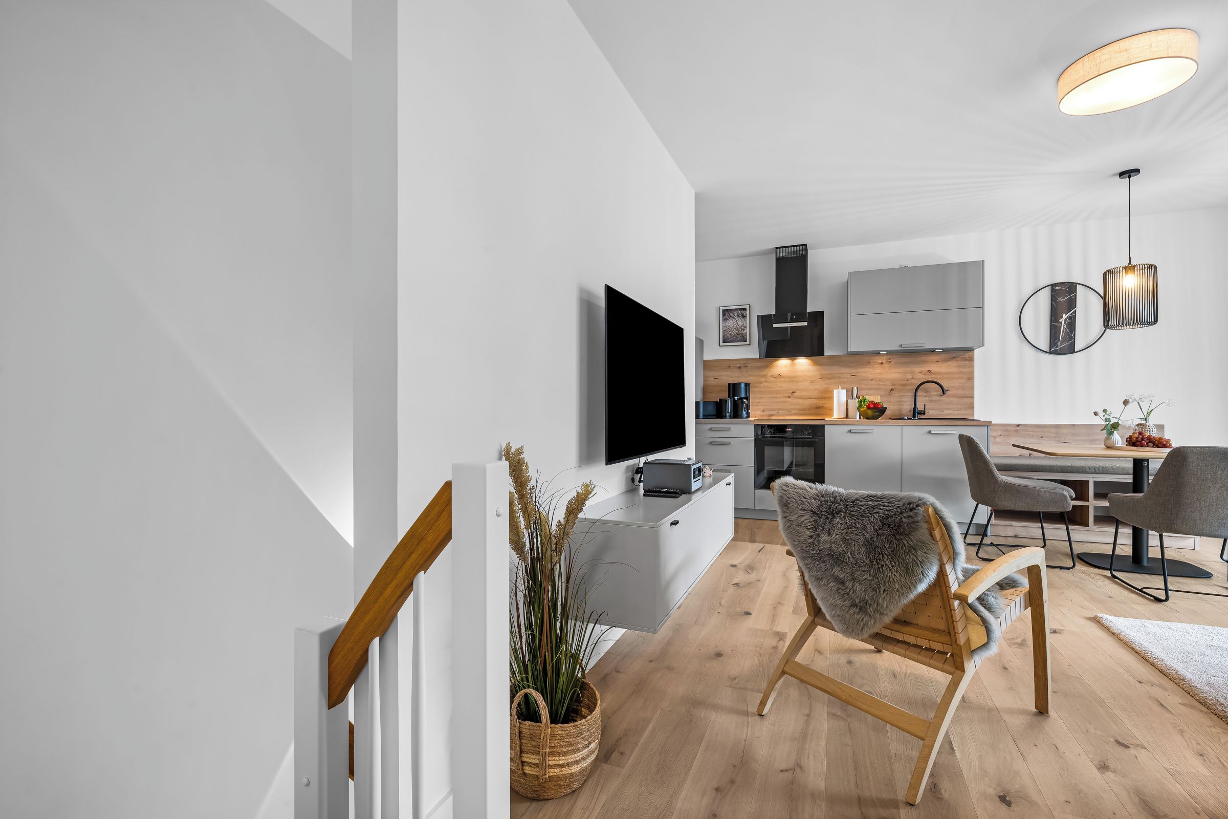 Eine moderne Küche mit Flachbildfernseher, Holzschränken und einem Essbereich mit einem grauen Stuhl und einem kleinen Tisch.