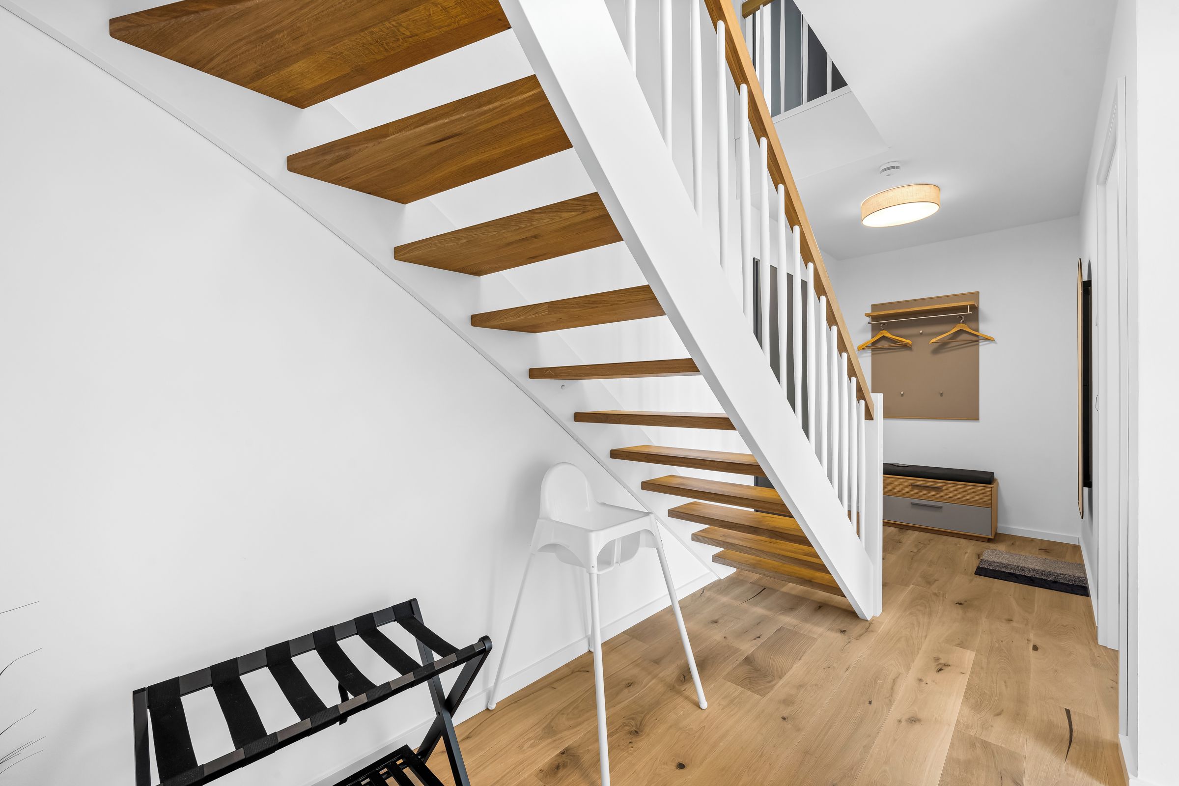 Ein modernes Interieur mit einer Holztreppe, weißen Wänden und einer Sitzecke mit einer Bank und einem Sessel.