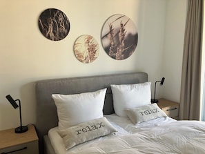 Ein Bett mit zwei Kissen, ein Nachttisch mit Lampe und Wandbild.