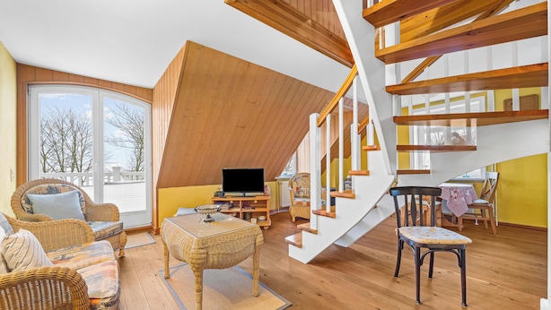 Ein geräumiger Wohnbereich mit einer Holztreppe, Korbmöbeln und einem Fernseher.