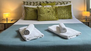 Ett hotellrum med en säng, gröna kuddar, en inramad tavla på väggen och ett fönster.